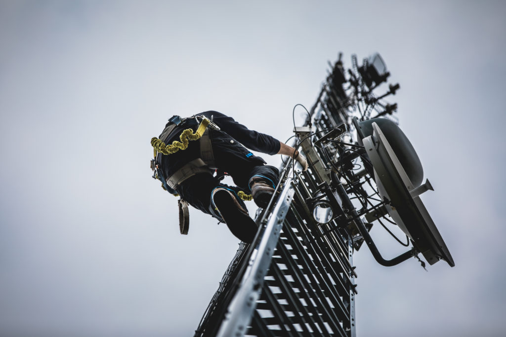 Telecom Worker Climbing Antenna Tower with Tools and Harness